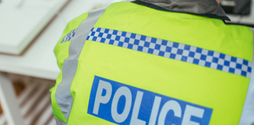 The back of a policeman, wearing a high-vis police jacket, sits at a desk.