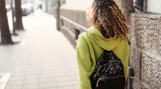 A young woman from the back, walking down the street with a backpack on in the sunshine.