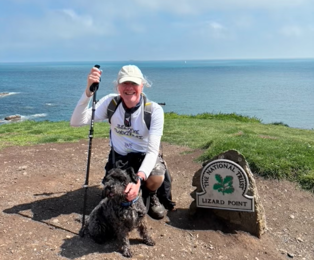 David Foster, an older caucasian man, kneeling on the grass at Lizard Point with his dog Pippin