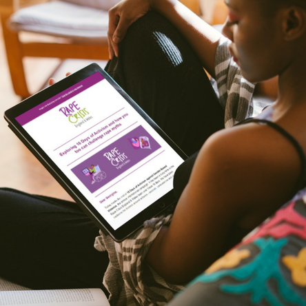 A woman sits on a sofa holding an iPad. The iPad is open on the Rape Crisis England and Wales newsletter