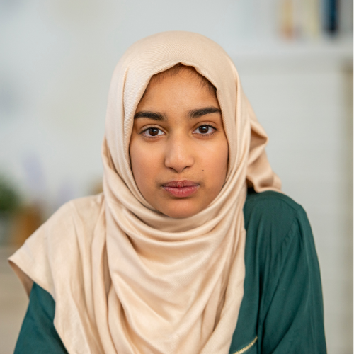 A teenage girl wearing a cream-coloured headscarf looks directly at the camera.