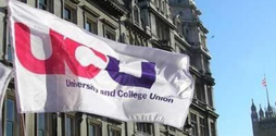 A white flag with the UCU logo on it stands billowing in the wind, with an old looking building behind it.