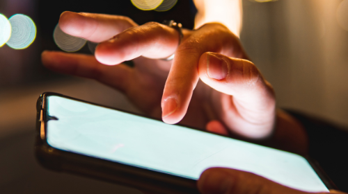 A young white person can be seen using a mobile phone. Only their hands are visible.