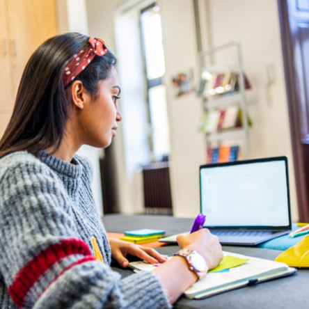 A young woman studies at a desk using a laptop.
