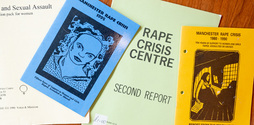 Reports and pamphlets from various points in the history of the UK Rape Crisis movement are shown laid out on a table.