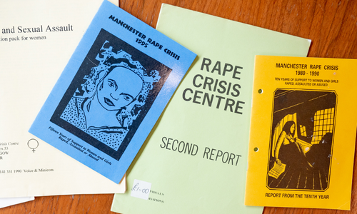 Reports and pamphlets from various points in the history of the UK Rape Crisis movement are shown laid out on a table.