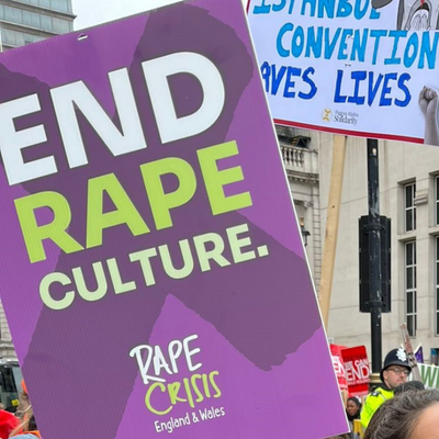 A Rape Crisis England & Wales placard reading 'END RAPE CULTURE.' is seen at the Million Women Rise march in London on 4th March 2023. In the background is a policeman and protesters.