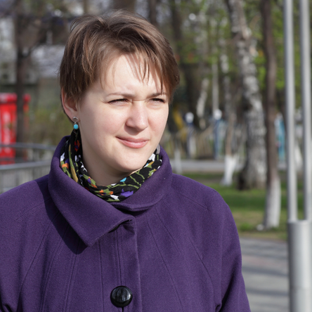 Woman outside in a purple coat looks thoughtfully into the distance.