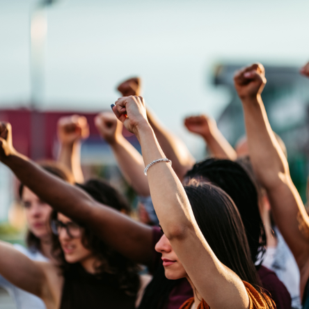 A group of women activists of different ethnicities raise their fists in the air.