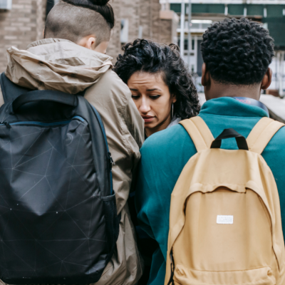 A young woman looks terrified as we see her confronted by two young men in the street. They have our backs to us so we can't see their faces.